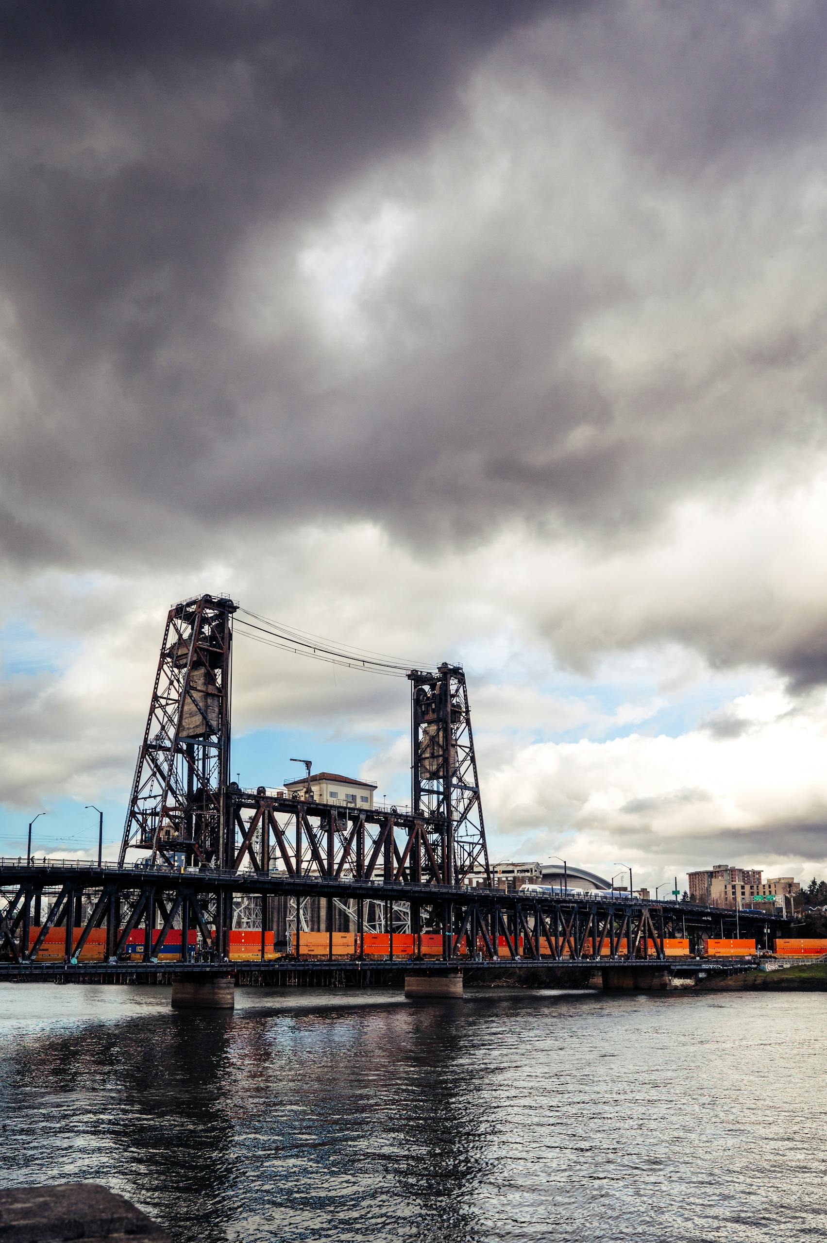 Scenic view of Steel Bridge crossing the Willamette River in Portland with dramatic clouds overhead.